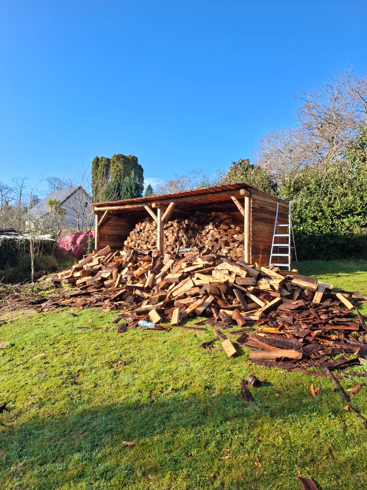 Abri à bois ouvert sur poteaux en bois rond, rempli de bois de chauffage fendu, à Quimper