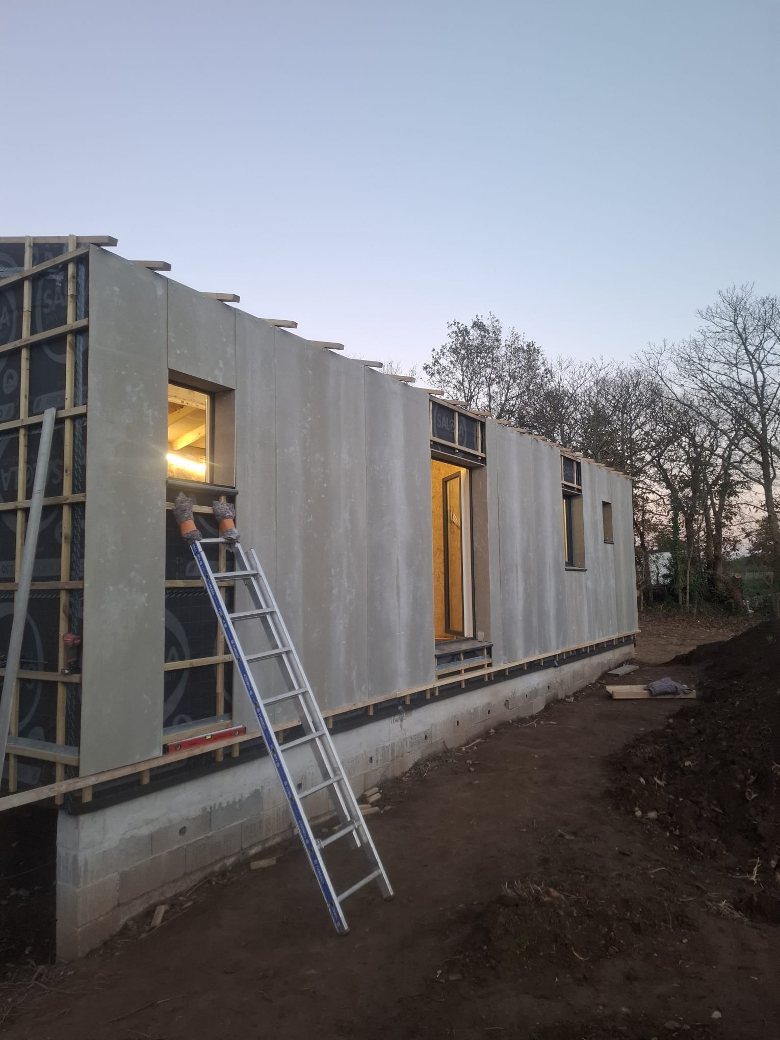 Longue façade en panneaux bois-ciment à l'aspect béton au crépuscule