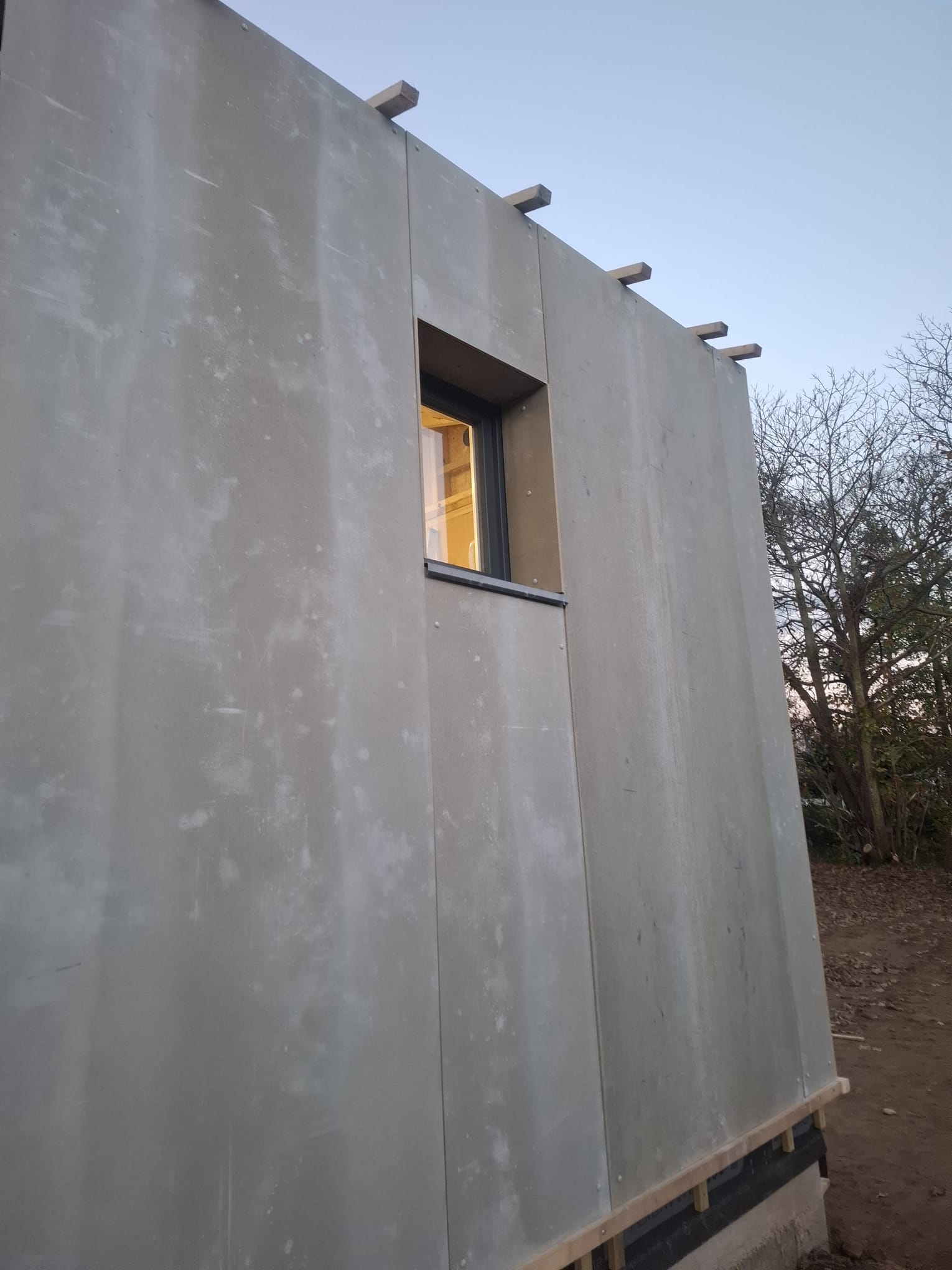 Détail d'un panneau bois-ciment à l'aspect béton et d'une fenêtre