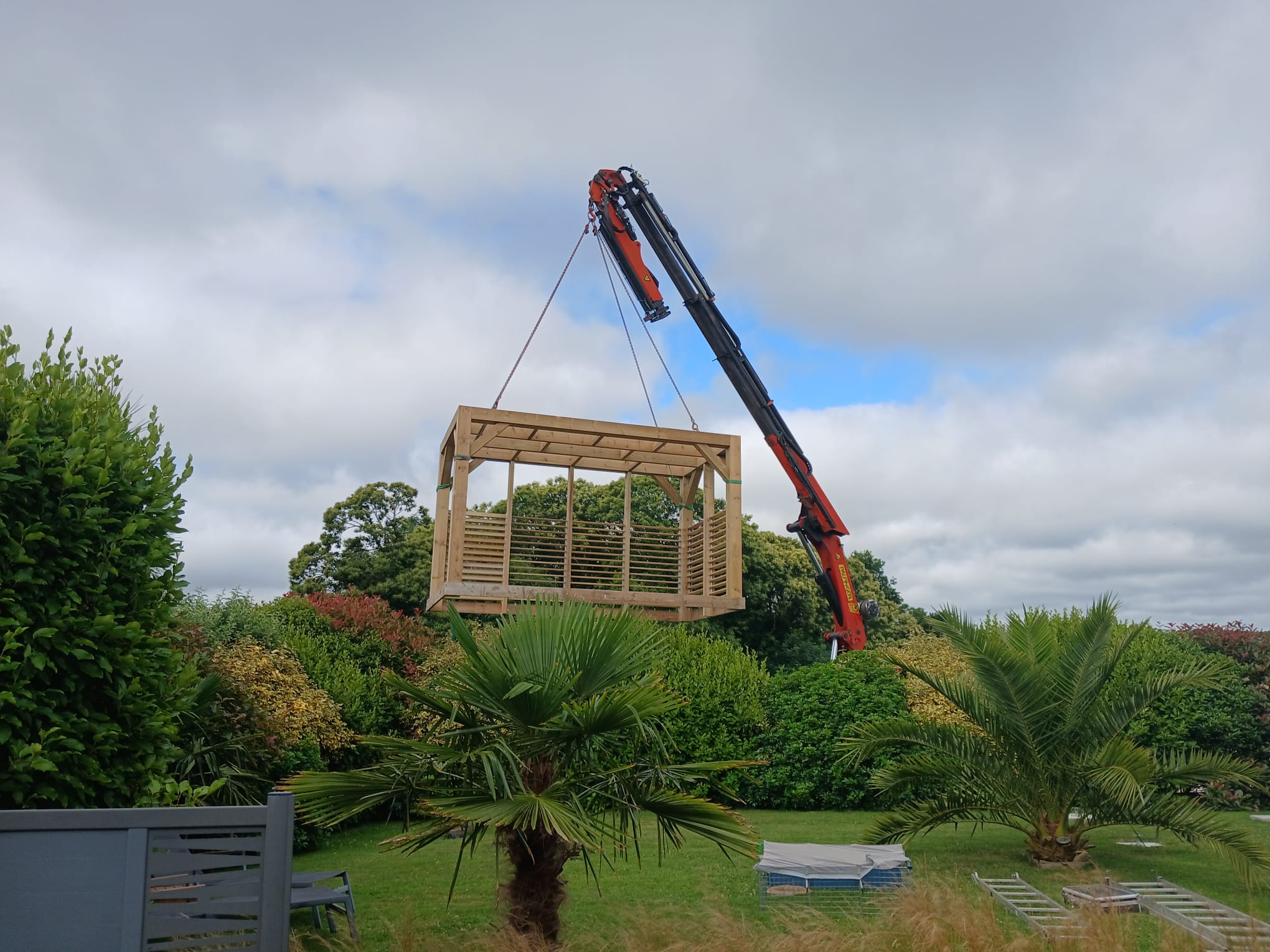 Pergola soulevée par une grue au-dessus du jardin lors de la pose