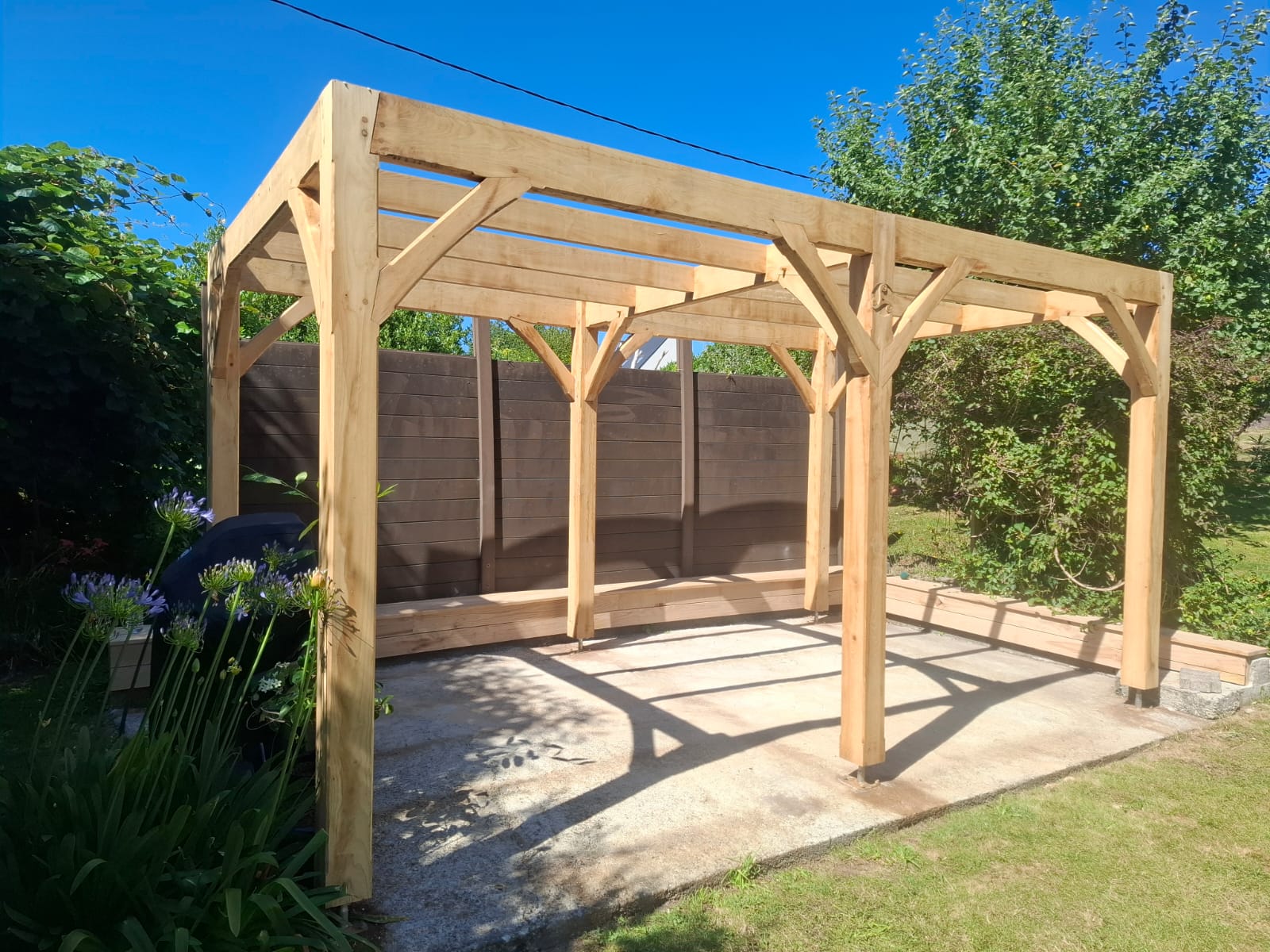 Pergola en châtaignier achevée dans le jardin, avec banc assorti en châtaignier
